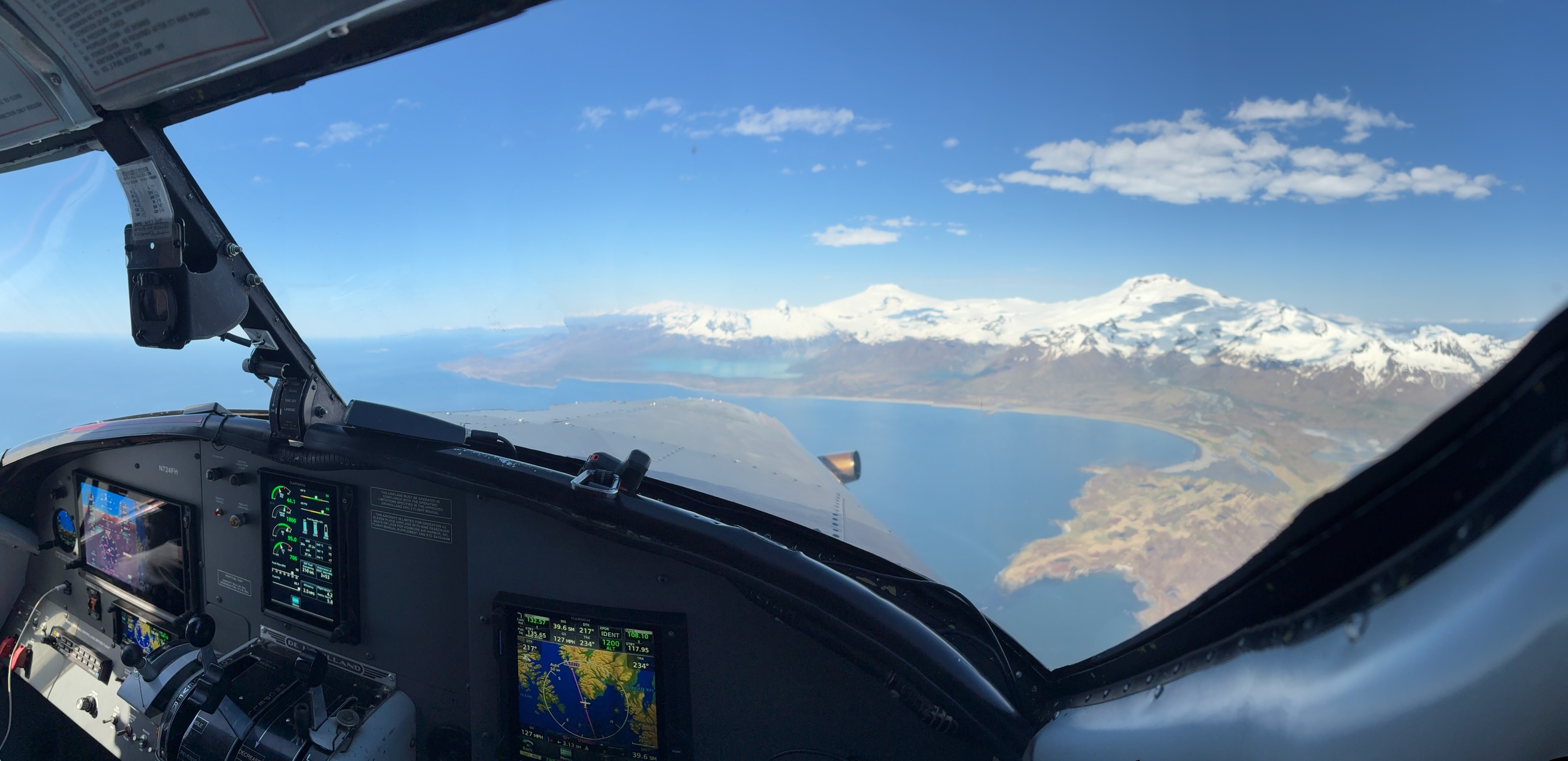 View from a float plane cockpit over Alaska — snow-capped mountains and coastal waterways below